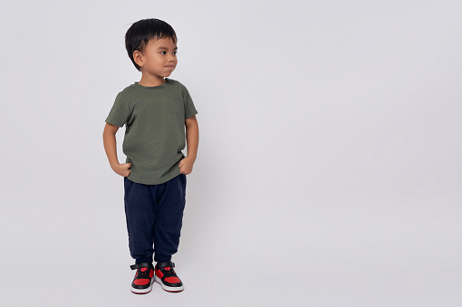 Full body little small smiling happy Asian boy 2-3 years old wearing a green t-shirt standing confident while looking at copy space isolated on white background