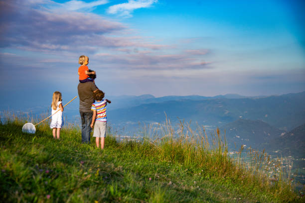 A young Asian boy in a red cap and a middle-aged Asian man in a plaid shirt ride a cable car in the mountains, enjoying a vacation view.