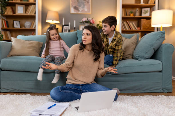 istock Small mischievous kids noising and distracting mother freelancer trying to concentrate on laptop and squeezing head working at table in light living room 2149348213