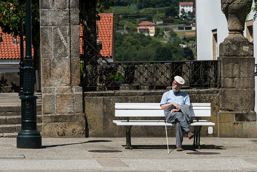 Betanzos, Spain - June 10, 2017: An older man sleeps peacefully in the sun, sitting on a bench in one of the streets of the village.