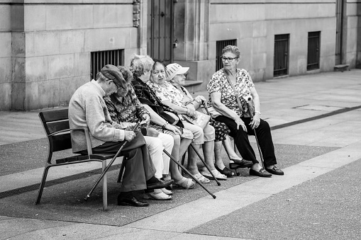 Pontevedra, Spain - July 14, 2018: A group of elderly people chat sitting on a wooden bench in the street.