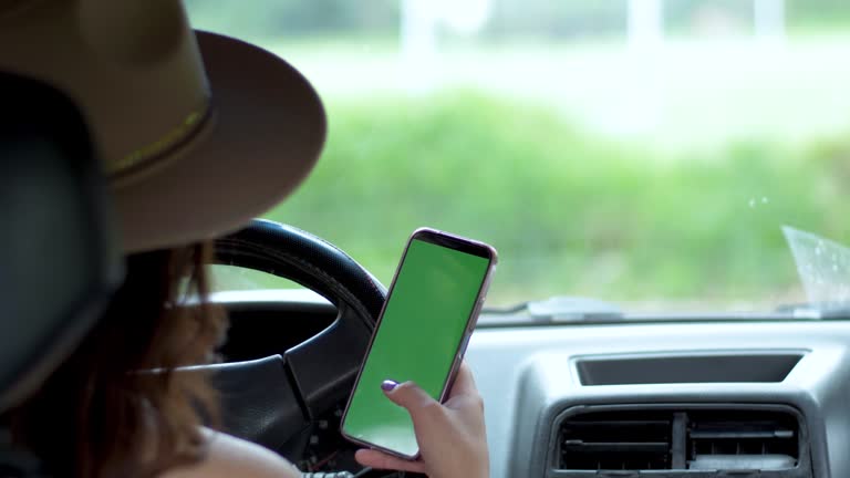 Over shoulder view of girl in car behind wheel scrolling on phone. Finding your way to your destination and making a final check before departure