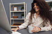 Love what you do concept. Joyful tanned adorable curly Latin businesswoman in linen shirt smiling look at monitor. Copy space. Attractive freelancer work from home office using modern desktop computer