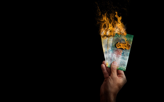 Swiss Franc banknotes burning flame held by hand on black background. Inflation money loss concept.