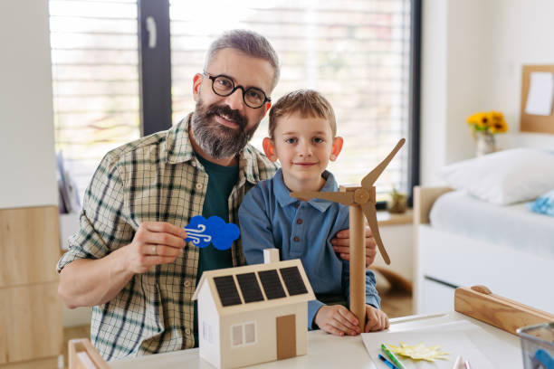 istock Father explaining renewable energy, teaching about sustainable lifestyle his young son. Playing with house with solar panels, wind turibine at home. 2149355679