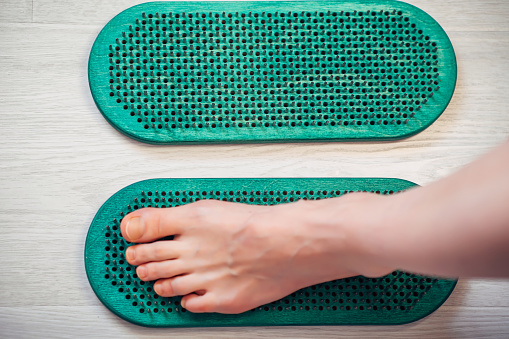 Close-up of Sadhu board with human foot. Feet standing on nails board. Yoga exercise and spiritual meditation practice desk. Alternative medicine and treatment.