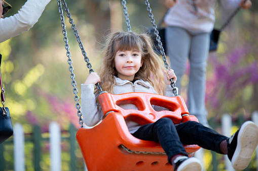 Happy blonde little girl swinging on a swing in the playground is having a lot of fun