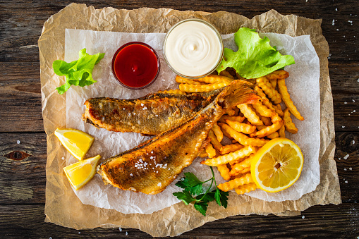 Fried perch with French fries and lemon served on paper on wooden background