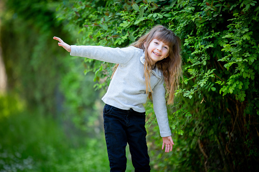 Cute little girl child having fun in nature. Green leaves in the background