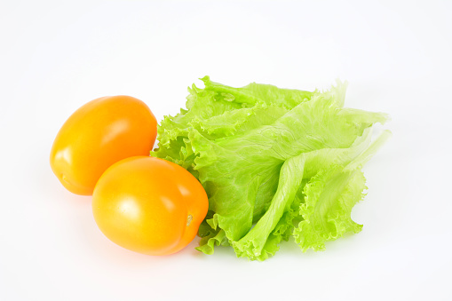 orange tomatoes with green salad leaves on white background