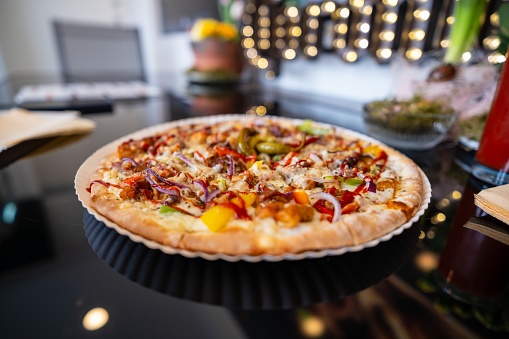 A Californiastyle pizza loaded with toppings such as pizza cheese, baked goods, and various ingredients is placed on a table. It is a delicious and satisfying fast food option