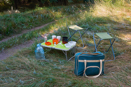 Tourist table with disposable tableware for a snack in nature. Picnic by the side of the road on green grass. Summer road trip.
