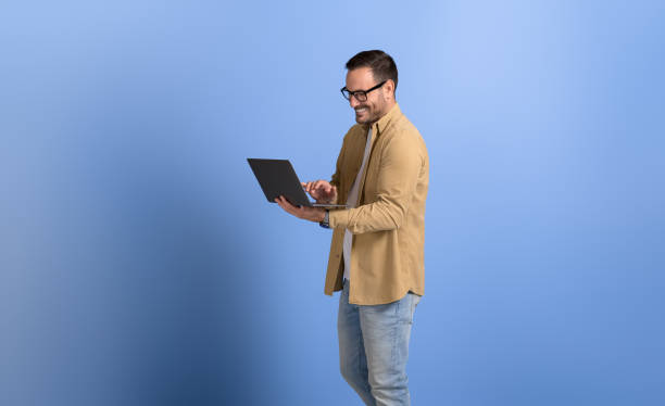 istock Male manager in eyeglasses smiling and working online over wireless computer against blue background 2149359308