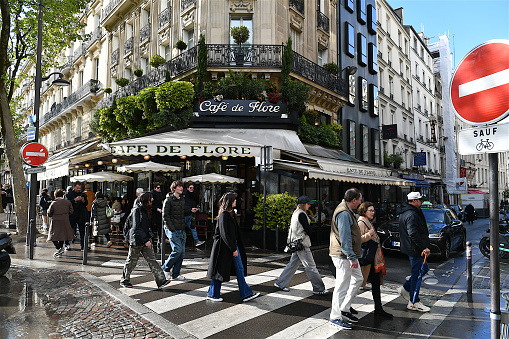 Paris, France-04 16 2024: Group of people passing in front of the Famous Café de Flore, located in the Saint-Germain-des-Prés district in Paris, France.