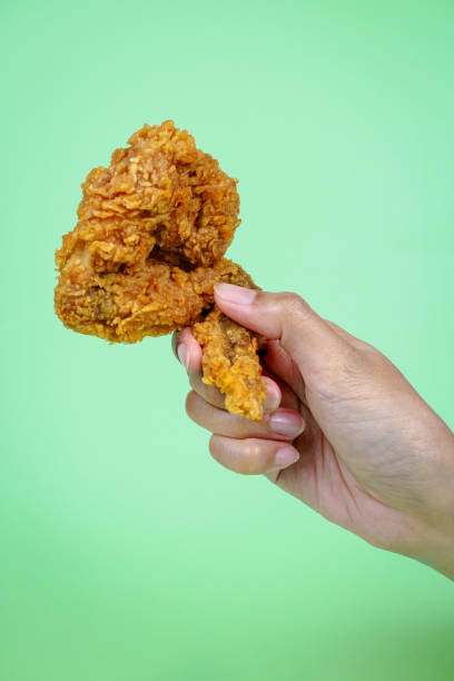 istock Female hand holding fried chicken on green background. 2149361434