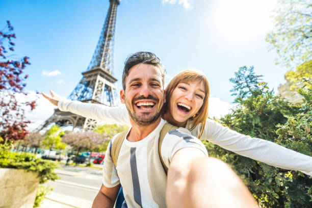 happy couple of tourists taking selfie picture in front of eiffel tower in paris, france - travel and summer vacation life style concept - stadje fotos stockfoto's en -beelden