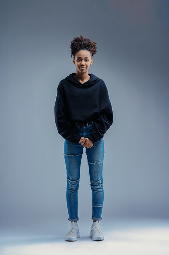 Wearing a dark hoodie and distressed jeans, the young woman poses with a relaxed, approachable demeanor