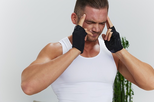 Man sports headache, migraine and dizziness from working out at home, pumped up man fitness trainer works out at home, the concept of health and body beauty. High quality photo