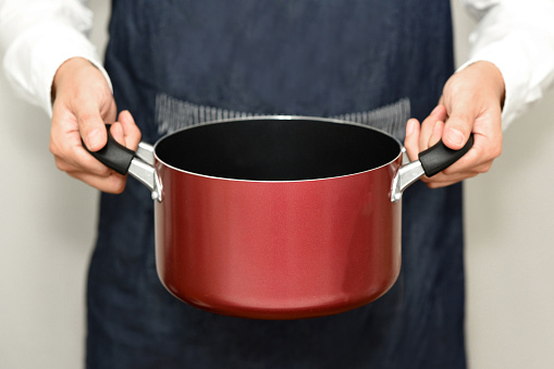 Hand of a man wearing an apron and holding a pot