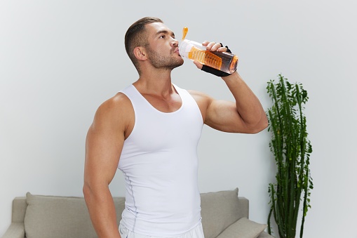 Man sports drinking water during break from workout, pumped up man fitness trainer works out at home, the concept of health and body beauty. High quality photo
