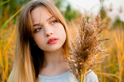 Beautiful young girl wearing blank gray t-shirt and black jeans posing against high green and yellow grass in early warm autumn. Outdoor portrait of beautiful female model.