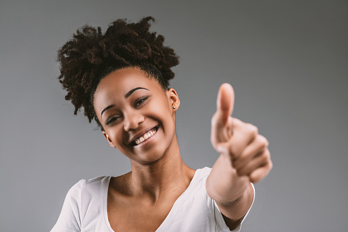 Radiant young woman in white, her afro hair and beaming smile complementing her enthusiastic thumbs up