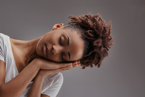Young woman in peaceful slumber, hands cradling face, embodies calm against a muted background