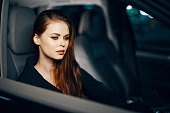 a stylish, luxurious woman is sitting in a black car at night in the passenger seat, and thoughtfully looks away. Safe driving topics