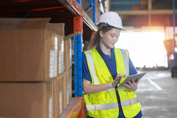 istock Female worker wearing safety uniform and hard hat using tablet checking inspect goods on shelves in warehouse. women worker check stock inspecting product in factory. 2149376792