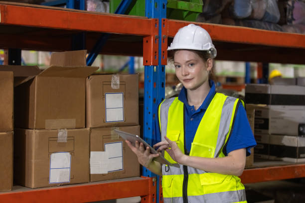 istock Female worker wearing safety uniform and hard hat using tablet checking inspect goods on shelves in warehouse. women worker check stock inspecting product in factory. 2149376799