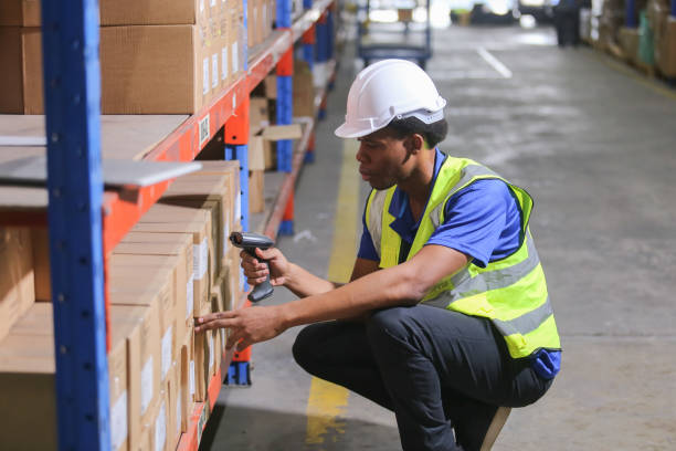 istock Man professional worker wearing safety uniform and hard hat worker scanning box inspect product on shelves in warehouse. Male worker is pointing finger inspecting product in factory. 2149376934