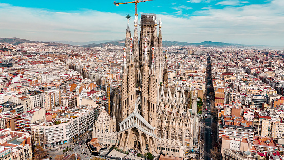 Aerial view of Sagrada Familia Cathedral in Barcelona, Catalonia, Spain, Aerial view of Barcelona Eixample residential area and Sagrada Familia Basilica, most famous travel destinations in europe\n\nThe Basílica i Temple Expiatori de la Sagrada Família, otherwise known as Sagrada Família, is a church under construction in the Eixample district of Barcelona, Catalonia, Spain. It is the largest unfinished Catholic church in the world. Designed by Catalan architect Antoni Gaudí (1852–1926), his work on Sagrada Família is part of a UNESCO World Heritage Site. On 7 November 2010, Pope Benedict XVI consecrated the church and proclaimed it a minor basilica.\nOn 19 March 1882, construction of the Sagrada Família began under architect Francisco de Paula del Villar. In 1883, when Villar resigned, Gaudí took over as chief architect, transforming the project with his architectural and engineering style, combining Gothic and curvilinear Art Nouveau forms. Gaudí devoted the remainder of his life to the project, and he is buried in the church's crypt. At the time of his death in 1926, less than a quarter of the project was complete.