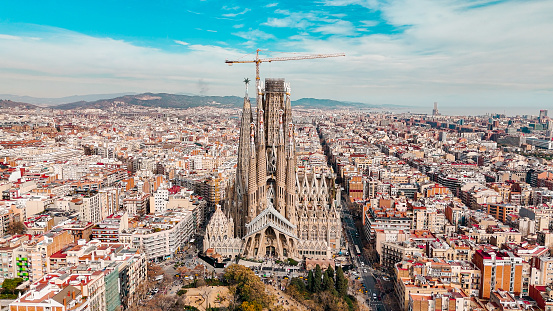 Aerial view of Sagrada Familia Cathedral in Barcelona, Catalonia, Spain, Aerial view of Barcelona Eixample residential area and Sagrada Familia Basilica, most famous travel destinations in europe\n\nThe Basílica i Temple Expiatori de la Sagrada Família, otherwise known as Sagrada Família, is a church under construction in the Eixample district of Barcelona, Catalonia, Spain. It is the largest unfinished Catholic church in the world. Designed by Catalan architect Antoni Gaudí (1852–1926), his work on Sagrada Família is part of a UNESCO World Heritage Site. On 7 November 2010, Pope Benedict XVI consecrated the church and proclaimed it a minor basilica.\nOn 19 March 1882, construction of the Sagrada Família began under architect Francisco de Paula del Villar. In 1883, when Villar resigned, Gaudí took over as chief architect, transforming the project with his architectural and engineering style, combining Gothic and curvilinear Art Nouveau forms. Gaudí devoted the remainder of his life to the project, and he is buried in the church's crypt. At the time of his death in 1926, less than a quarter of the project was complete.