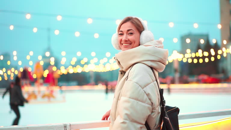 Woman in warm clothes smiling at camera outside ice rink during Christmas