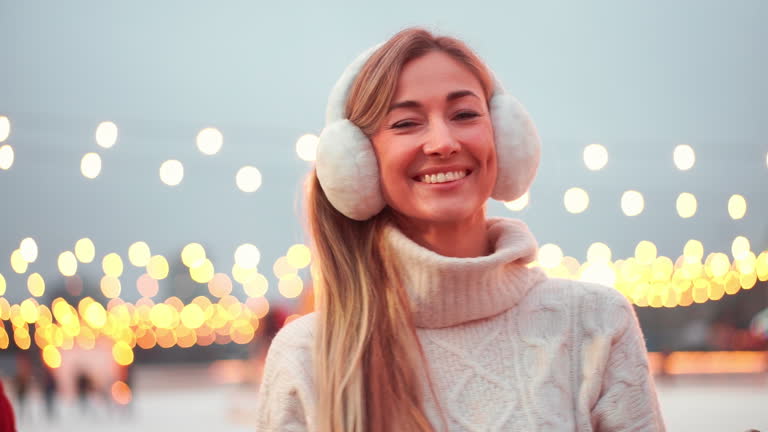 Woman in earmuffs standing outside ice rink and smiling at camera