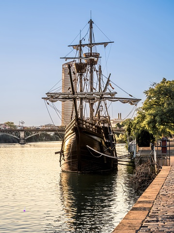 The Nao Victoria replica carrack ship docked at the Guadalquivir River in the historic central downtown area of Seville, Spain, sunset golden hour