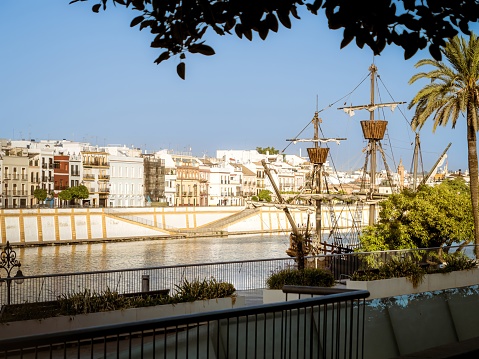 The Nao Victoria replica carrack ship docked at the Guadalquivir River in front of the houses of Triana district of Seville, Spain, sunset golden hour