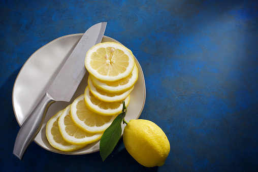 Close up of lemon slices on a ceramic dish on a blue kitchen countertop.