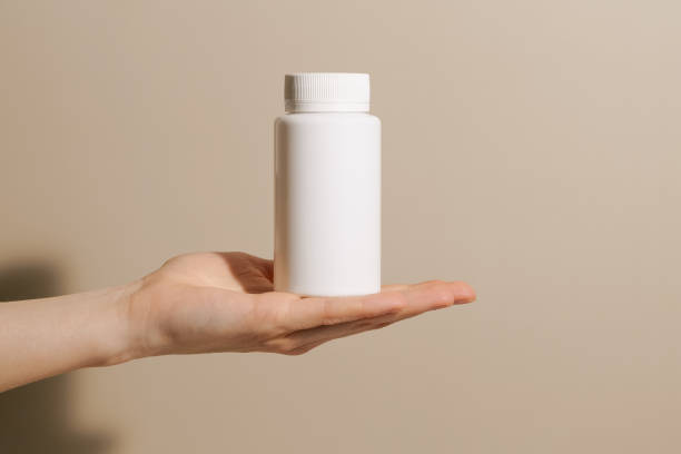 istock Female hand holding white plastic mockup pill jar on beige isolated background. Concept of pharmacy, medicine, natural dietary supplements, health care. 2149388270