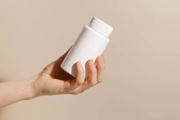 istock Female hand holding white plastic mockup pill jar on beige isolated background. Concept of vitamins for beauty and health, dietary supplements and pharmacy. 2149388271