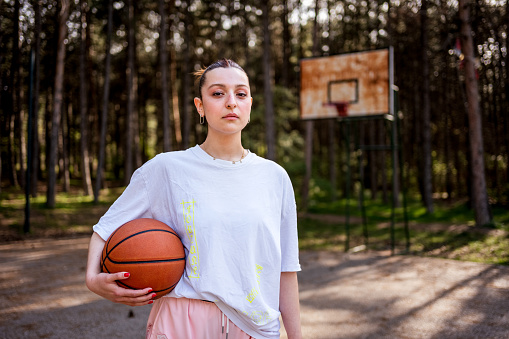 Portrait of a young woman holding a basketball and looking at camera serious on a sport court