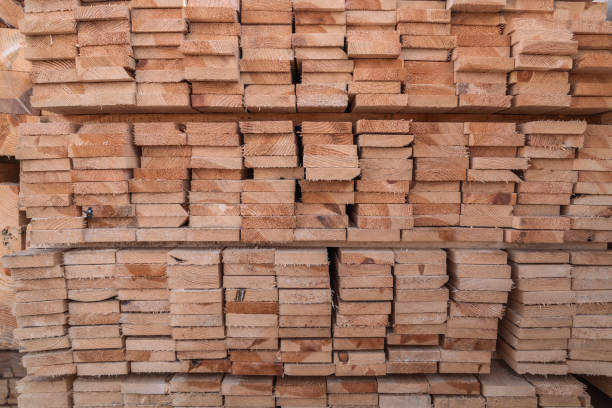 Stacks of neatly arranged wooden planks rest at a lumberyard, showcasing the natural texture and color of the wood in daylight.