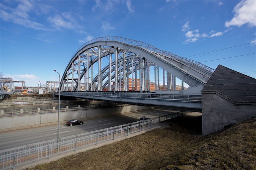 An arched bridge over an urban road with a car on a clear day.\nё