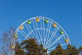 A Ferris wheel with bright cabins against the backdrop of a blue sky and treetops.
