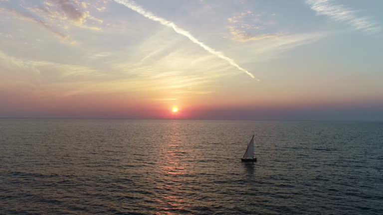 Drone Shot of a Man Sailing an Old Boat Alone on the Sea at Sunset. Concept of Freedom, Travel, Loneliness, Timelessness, Exploration, Solitude, Adventure, Serenity, Medieval Boat