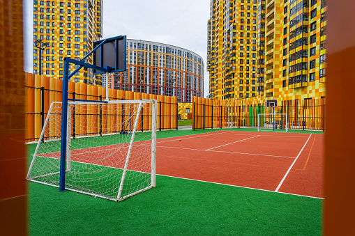 A sports ground with soccer goals and a basketball hoop against the backdrop of colorful residential high-rises.