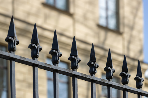 Decorative spikes of a wrought iron fence against the facade of a building.