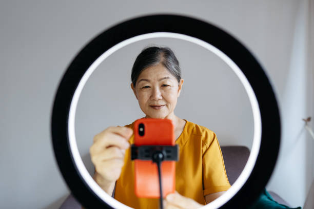 istock Senior woman setting up smartphone on ring light for live streaming. Retirement lifestyle. Active senior using smartphone for content creation or social media live broadcast at home. 2149398035