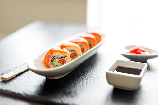 Close up image of sushi roll covered with fresh salmon on the slate board.