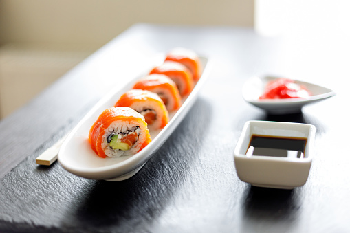 Close up image of sushi roll covered with fresh salmon on the slate board.